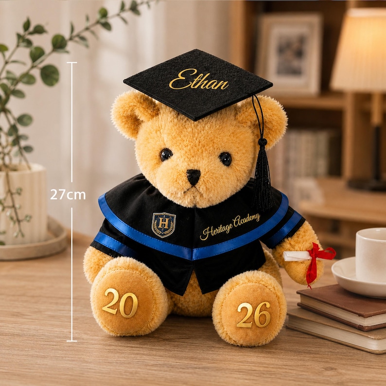 Puede incluir: Un oso de peluche marr&oacute;n dorado con un gorro de graduaci&oacute;n negro con el nombre "Ethan" en letras doradas. El oso viste una toga de graduaci&oacute;n negra y azul y sostiene un diploma enrollado con una cinta roja. El oso mide 27 cm de alto.