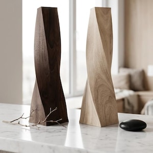 Puede incluir: Dos esculturas de madera altas y verticales con un diseño geométrico retorcido. Una escultura está hecha de madera marrón oscura con veta visible, mientras que la otra es de madera clara con un patrón de veta natural. Ambas tienen una base plana.