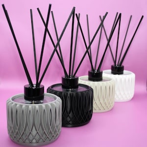 May include: Four reed diffusers arranged in a row, featuring cylindrical containers with a textured, geometric lattice pattern. The containers are colored gray, black, off-white, and white, each topped with a black cap and several black reeds.