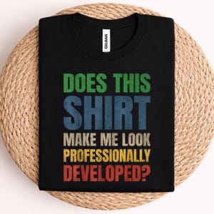May include: A black short-sleeved t-shirt with a Gildan label at the neck. The front features multi-colored distressed text that reads: DOES THIS SHIRT MAKE ME LOOK PROFESSIONALLY DEVELOPED? The words are stacked in green, blue, tan, yellow, and red.