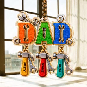 May include: A personalized "DAD" keychain with orange, green, and blue letters, each featuring a wrench. Below, three hammers with wrenches and names: "KRISTY", "WINNIE", and "BENJI". The keychain is suspended by a gold chain.