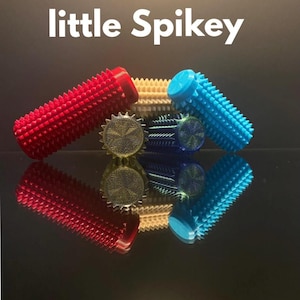 May include: A selection of colourful, spiky massage rollers are displayed. The rollers are red, yellow, and blue, and are arranged on a reflective surface. The text "little Spikey" is at the top of the image.