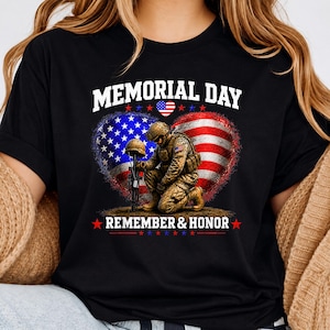 May include: Black t-shirt with a Memorial Day design. The graphic features a soldier kneeling before a helmet and rifle, set against a heart-shaped American flag. The words "MEMORIAL DAY" and "REMEMBER & HONOR" are displayed in white.