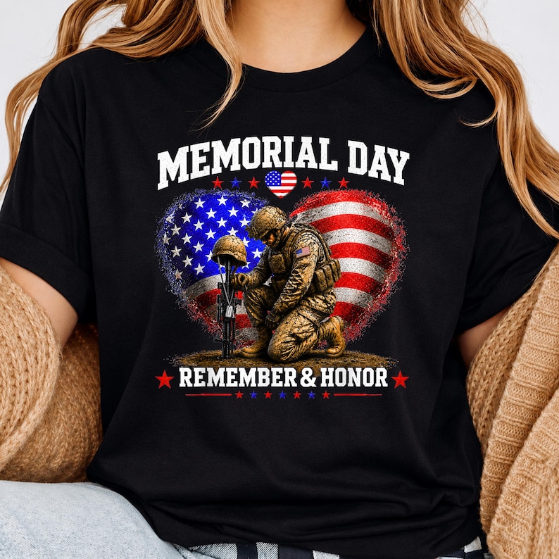 May include: Black t-shirt with a Memorial Day design. The graphic features a soldier kneeling before a helmet and rifle, set against a heart-shaped American flag. The words "MEMORIAL DAY" and "REMEMBER & HONOR" are displayed in white.