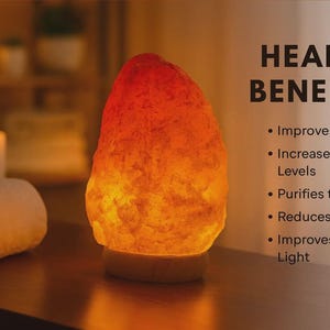 Puede incluir: Una lámpara de sal del Himalaya brillante con un degradado de colores naranja y amarillo. La lámpara está sobre una base de madera, junto a una toalla blanca enrollada. El texto enumera los beneficios para la salud.
