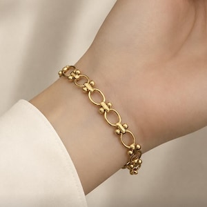 May include: A gold bracelet with a chain-link design, featuring oval links and decorative elements. The bracelet is displayed on a wrist, highlighting its polished finish and intricate details. A classic piece of jewellery.