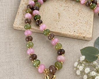 May include: A beaded necklace featuring alternating round pink, olive green, and dark brown beads separated by small gold-toned spacers. The necklace includes a single gold-toned letter K pendant hanging from the centre of the beaded strand.