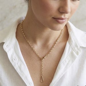 May include: A gold-toned necklace featuring a circular link chain design. The necklace includes a central clasp mechanism that allows a short segment of the chain to hang vertically, ending in a small, teardrop-shaped loop attachment.