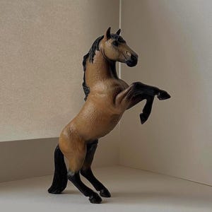 May include: A brown and black horse figurine rearing up on its hind legs. The horse has a tan body, black mane and tail, and black legs. The figurine is a detailed representation of a horse.