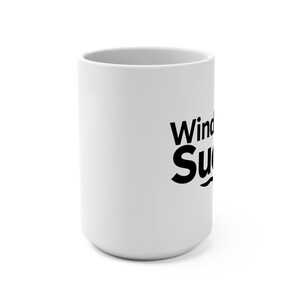 Puede incluir: Una taza de cerámica blanca con las palabras "Wind Sucks" impresas en letras negras en negrita. La taza tiene forma cilíndrica y un diseño sencillo y limpio, apto para bebidas frías o calientes.