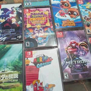 May include: A selection of Nintendo Switch game cases, featuring titles such as "Super Mario Odyssey", "Animal Crossing", and "Pokemon Scarlet Violet". The cases are in clear plastic, displaying vibrant game artwork and titles.