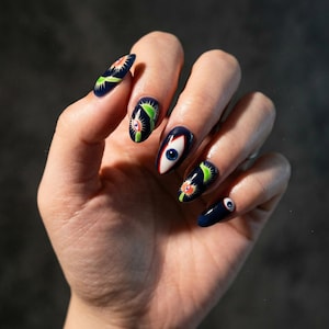 May include: Dark blue nail art featuring various designs. Some nails showcase a vibrant eye design with a blue iris, while others display a green and orange plant-like motif. The nails are painted with a glossy finish.