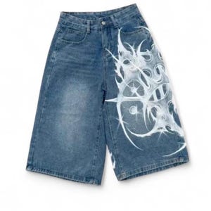 Puede incluir: Pantalones cortos vaqueros azul claro con un diseño abstracto blanco único en la pierna derecha. Los pantalones cortos tienen un diseño clásico de cinco bolsillos y cierre de botón y cremallera. Los pantalones cortos son de corte holgado.