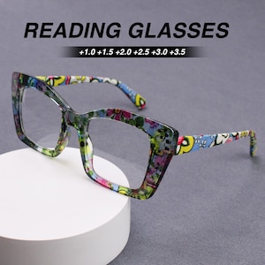 May include: Reading glasses with a thick, square-shaped frame featuring a colorful floral pattern in shades of blue, green, yellow, and pink. The text READING GLASSES and +1.0 +1.5 +2.0 +2.5 +3.0 +3.5 are printed above the eyewear.