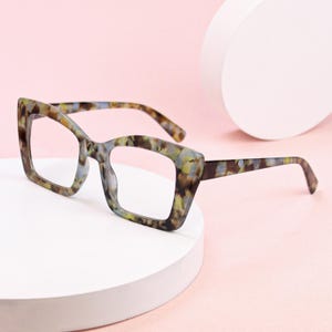 May include: Oversized square eyeglasses featuring a multi-colored tortoiseshell pattern in shades of brown, blue, and yellow. The frames have a thick, bold rim design with matching patterned temples, providing a distinct look with clear lenses.