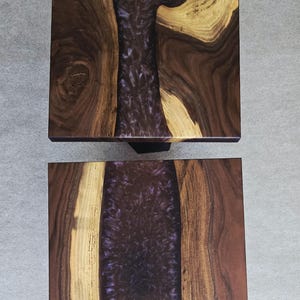 May include: Two square wooden tables with a dark brown wood grain and a central river of deep purple resin. The tables are set against a neutral gray background, showcasing the natural wood patterns and the glossy resin.