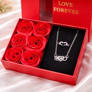 May include: A red gift box containing six red rose soaps and a silver necklace and ring set. The necklace and ring have heart-shaped designs. The box lid displays "LOVE FOREVER" in gold lettering.