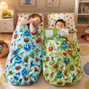 May include: Two children lying in sleeping bags with Dr. Seuss character prints. One sleeping bag is light blue and the other is light green, both featuring colorful circular patterns. One child is reading a book titled People House.