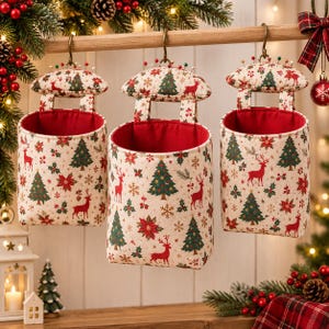 May include: Three cylindrical fabric hanging organizers with a cream background featuring a repeating pattern of red reindeer, green Christmas trees, and red poinsettias. Each organizer has a red interior lining and a padded top with pins.