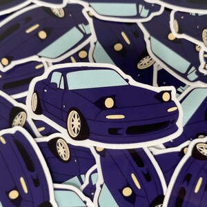 May include: A sticker of a navy blue sports car with pop-up headlights and white wheels. The car is illustrated in a cartoon style, with a light blue background. The stickers are scattered across the image.