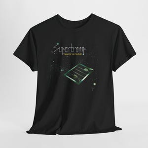 May include: A black short-sleeved t-shirt featuring a graphic print of the Supertramp Crime of the Century album cover. The design displays a green-tinted window with hands reaching through bars against a dark, starry space background.
