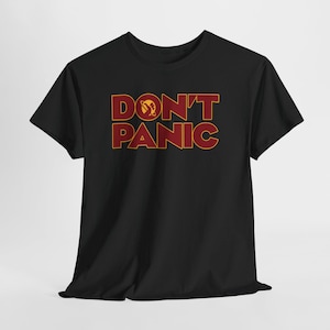 May include: Black t-shirt with the words "DON'T PANIC" in a bold, red and gold font. The design includes a planet graphic above the letter "O". The shirt is made of a soft material.