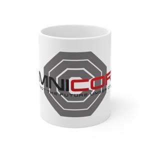 Op de afbeelding: Witte keramische koffiemok met de tekst "OMNICOR" in zwart en rood, met een grijs geometrisch ontwerp. De mok heeft ook de tekst "GOT THE FUTURE UNDER CO".