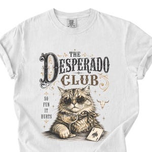 Könnte beinhalten: Weißes T-Shirt mit einer Grafik einer Katze mit Sonnenbrille, die ein Weinglas und eine Spielkarte hält. Der Text lautet "The Desperado Club" und "So Fun It Hurts" in einem Vintage-Stil.
