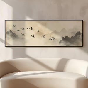 Puede incluir: Una pieza de arte mural rectangular en un marco negro que presenta una pintura de paisaje horizontal. La obra muestra una bandada de aves oscuras volando sobre un fondo beige brumoso con siluetas de montañas en tonos gris suave.
