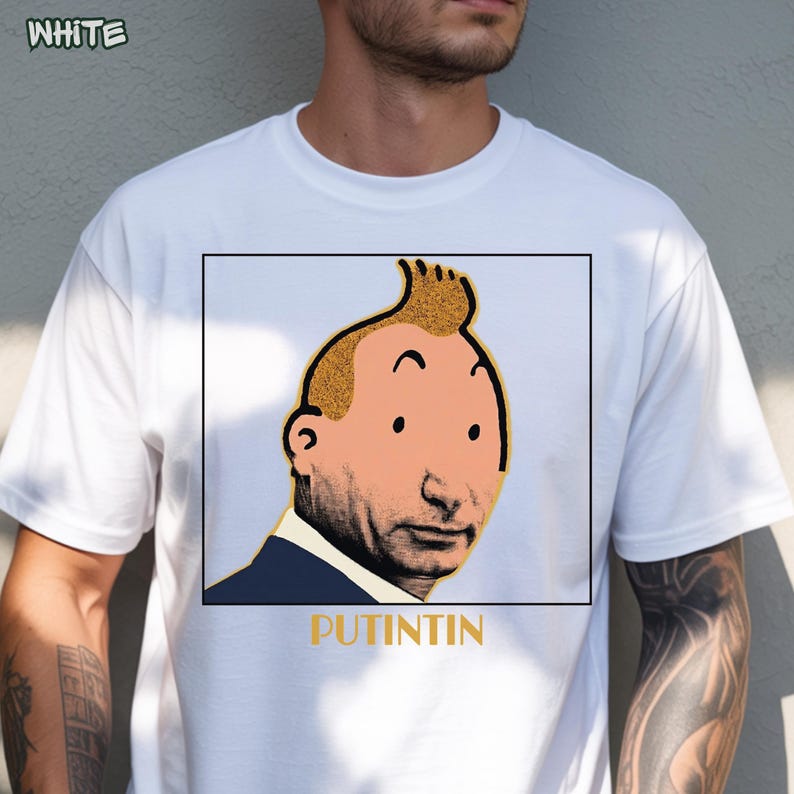 May include: A white short-sleeved t-shirt featuring a square graphic print of a stylised face with a yellow tuft of hair and a dark blue suit collar. Below the graphic, the text PUTINTIN is printed in yellow capital letters.
