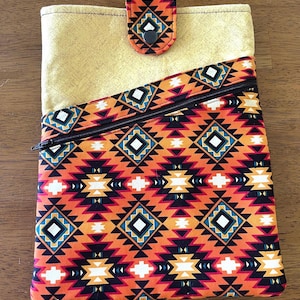 May include: A rectangular fabric pouch featuring a vibrant orange, black, white, and teal geometric pattern. The pouch includes a diagonal zippered pocket on the front and a solid mustard yellow top section secured by a matching patterned flap with a black snap.