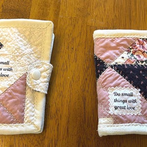 May include: Two rectangular quilted fabric cases featuring a patchwork design in shades of pink, cream, and dark floral patterns. Each case has a white snap closure and a white fabric label printed with the text Do small things with great love.