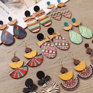 Può includere: Una collezione di orecchini in legno colorati con vari disegni geometrici e fantasia. Gli orecchini presentano un mix di forme, tra cui gocce, ovali e semicerchi, con accenti neri, marroni e dorati.