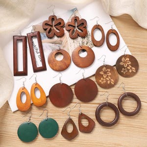 Puede incluir: Una colección de pendientes de madera en varias formas y colores. Los estilos incluyen diseños rectangulares, ovalados, circulares y florales. Los pendientes son en tonos marrón, naranja y verde, con ganchos plateados.