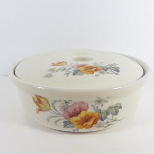 May include: A white ceramic casserole dish with a lid. The dish and lid are decorated with a floral pattern in shades of yellow, orange, pink, and green.