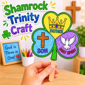 Könnte beinhalten: Ein farbenfrohes Shamrock Trinity Craft, gehalten von einer Hand, zeigt ein Kleeblatt-Design mit den Worten "Vater", "Sohn" und "Heiliger Geist". Das Bastelprojekt enthält einen Holzstab und ist mit einer Krone, einem Kreuz und einer Taube verziert. Die Worte "Shamrock Trinity Craft" stehen oben.