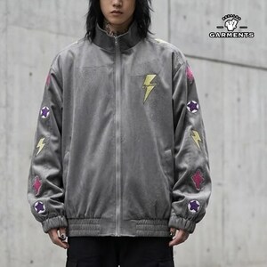 May include: A gray zip-up jacket with a high collar. The jacket features yellow lightning bolt patches and colorful star and lightning bolt patches on the sleeves. The brand logo "REZALOO GARMENTS" is visible in the upper right corner.