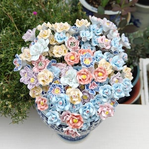 May include: A ceramic floral arrangement in a blue and white patterned vase. The flowers are in shades of pink, yellow, blue, and white. The arrangement is dense and full, with many individual flower blooms visible.