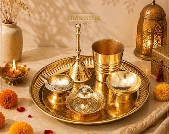 Può includere: Un set religioso in ottone dorato, tra cui un vassoio, una campana, una tazza e piccole ciotole. Il set è disposto con una candela accesa, fiori e una lanterna decorativa. Gli oggetti sono esposti su una superficie chiara.