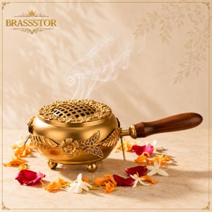 May include: A gold-toned brass incense burner with a wooden handle, featuring a decorative lid with a lattice pattern and floral motifs. The body is adorned with metal butterfly and leaf accents, resting on small feet with wisps of smoke rising.