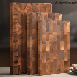 May include: Three wooden chopping boards of different sizes, arranged vertically. They are made of dark brown wood with a mosaic pattern. The boards have rounded corners and a smooth surface, suitable for food preparation.