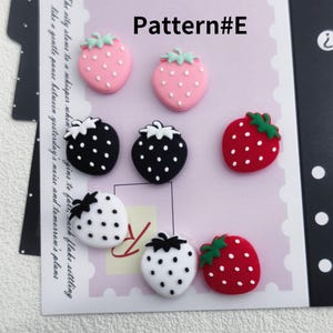 May include: A collection of strawberry-shaped embellishments in various colors. The image includes pink, black, white, and red strawberries with white dots and green stems. The text "Pattern #E" is visible at the top.