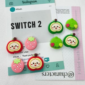 May include: A collection of eight colorful silicone charms featuring cartoon fruit characters with faces. The set includes red apples, pink strawberries, and green lime-like shapes, all arranged on a white card with Instagram-style text.