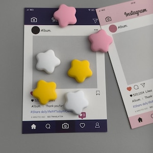 May include: A collection of star-shaped magnets in pink, white, and yellow, scattered on and around Instagram-themed photo frames. The frames are white and pink, with social media interface elements. The text "Album. Thank you for!" is visible.