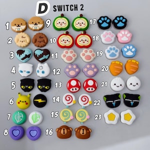 May include: A collection of colorful joystick caps for a gaming console. The caps feature various designs, including animal faces, paw prints, food items, and other cute graphics. The caps are in various colors, including brown, blue, and yellow.