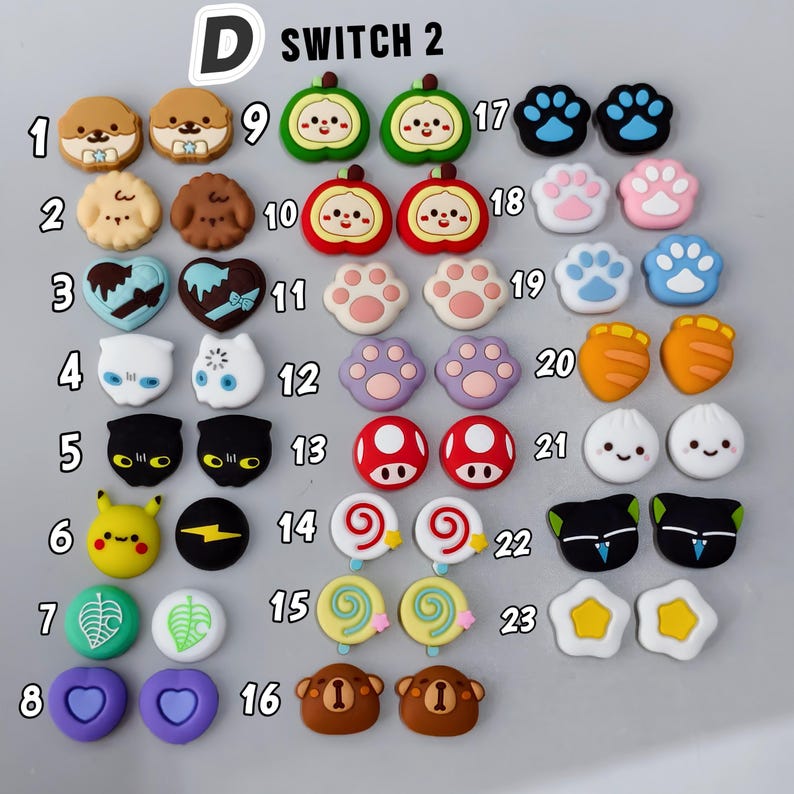 May include: A collection of colorful joystick caps for a gaming console. The caps feature various designs, including animal faces, paw prints, food items, and other cute graphics. The caps are in various colors, including brown, blue, and yellow.