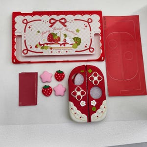Puede incluir: Un conjunto de fundas protectoras para consola de juegos en rojo y blanco con un gráfico de fresa y pastel y el texto Spring Special Strawberry. Incluye dos fundas para mandos, cuatro tapas de botones pequeñas de fresa y estrella y dos láminas adhesivas.