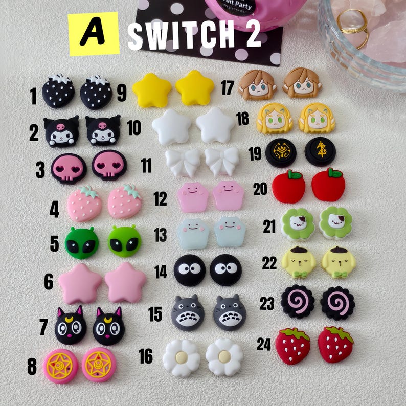 May include: A collection of colorful, cartoon-style charms, including strawberries, stars, and character faces. The charms are in various colors like pink, yellow, and black. The text "A SWITCH 2" is visible at the top.