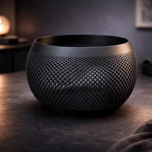 May include: A black, spherical decorative bowl with a lattice design. The bowl sits on a dark surface, with a soft, dark gray cloth in the foreground. The overall theme is modern home decor.