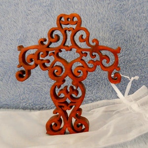 Könnte beinhalten: Ein Holzkreuz mit einem dekorativen, komplizierten Design. Das Kreuz ist aus dunkelbraunem Holz gefertigt und hat eine Herzform in der Mitte.